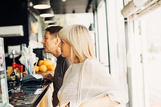 An adult mature happy couple in love in a street cafe order coffee. A blonde caucasian man and woman spend time together. Senior wife and husband walking outdoors