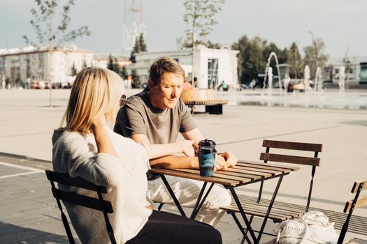 An adult mature happy couple in love in a street cafe order coffee. A blonde caucasian man and woman spend time together. Senior wife and husband walking outdoors