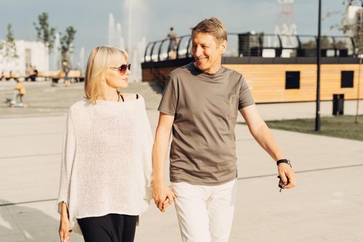 An adult mature happy romantic couple in love outdoors in city street park. A blonde caucasian man and woman spend time together. Senior wife and husband walking outside on town square