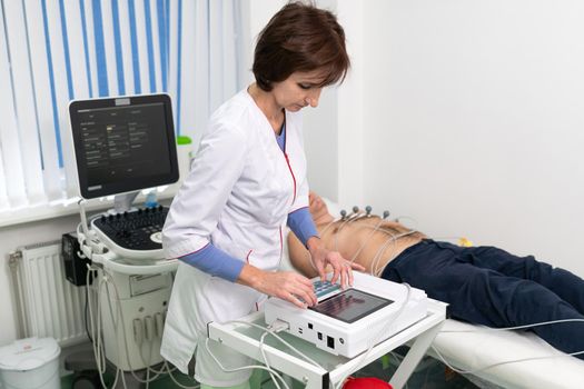 Cardiologist doctor performs electrocardiography procedure on man lying on couch in hospital. ECG test of male at modern clinic. Diagnostic, healthcare, medical service. Hospital patient and EKG test.