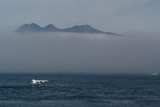 A Float Plane Taxis Through the Water in Tofino on Vancouver Island in Canada surrounded by low hanging clouds. High quality photo