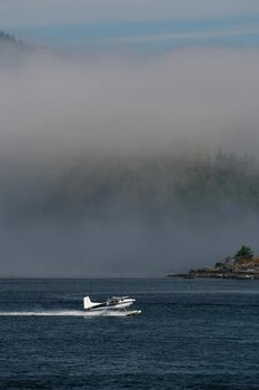 A Float Plane Accelerates for Takeoff in Tofino on Vancouver Island in Canada surrounded by low hanging clouds. High quality photo