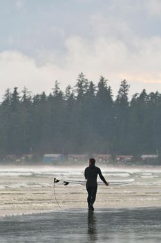 A Surfer Carries his Board Along the Beach in Tofino British Columbia in Canada. High quality photo