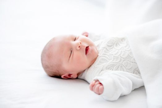 Adorable newborn baby girl wearing white costume lying in the bed and sleeping with mouth open. Cute infant child napping at home