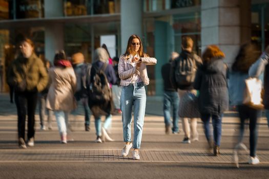 Young woman walking in the middle of crowded street and looking time at hand watches. Big city life. High quality photo