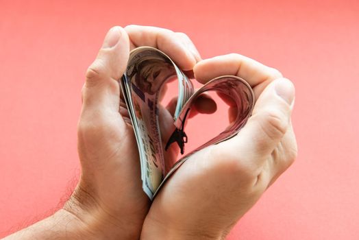 several 100 dollar bills folded in the shape of a heart in male hands. love of money, greed, business, wealth.