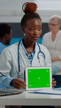 African american medic talking about green screen technology on tablet sitting at desk with old patient. Black doctor vertically holding mockup template and isolated background with chroma key