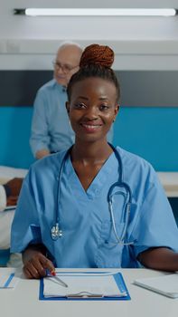 Close up of woman working as nurse sitting at desk and reading documents, files, papers of patient checkup. Person wearing uniform and stethoscope in healthcare cabinet at facility