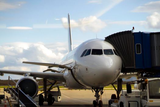 A passenger air plane is parked on the territory of the airport near the runway in the evening, baggage is loading, view through the gate to board the flight before departure.