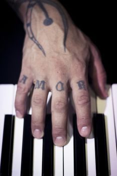 Tattooed mans hands on the keyboard of a piano. Dark background