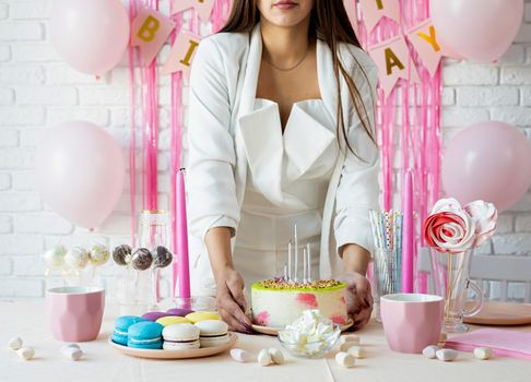 Birthday party. Birthday tables. Attractive woman in white party clothes preparing birthday table with cakes, cakepops, macarons and other sweets