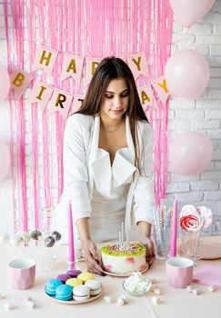Birthday party. Birthday tables. Attractive woman in white party clothes preparing birthday table with cakes, cakepops, macarons and other sweets