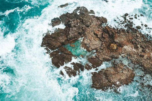 Aerial drone shot of ocean waves around island of rocks and rock pool