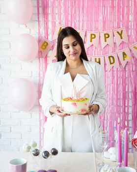 Birthday party. Birthday tables. Attractive woman in white party clothes preparing birthday table with cakes, cakepops, macarons and other sweets