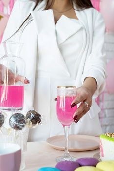 Birthday party. Birthday tables. Attractive woman in white party clothes preparing birthday table with cakes, cakepops, macarons and other sweets, having drink