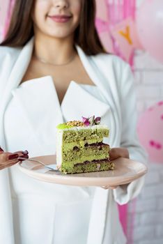 Birthday party. Birthday tables. Attractive woman in white party clothes preparing birthday table, celebrating and holding a piece of pistachio cake