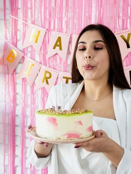 Birthday party. Birthday tables. Attractive woman in white party clothes preparing birthday table with cakes, cakepops, macarons and other sweets, blowing the candles