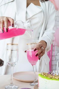 Birthday party. Birthday tables. Attractive woman in white party clothes preparing birthday table with cakes, cakepops, macarons and other sweets, having drink