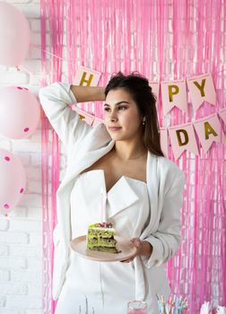 Birthday party. Birthday tables. Attractive woman in white party clothes preparing birthday table, celebrating and holding a piece of pistachio cake