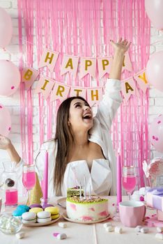 Birthday party. Birthday tables. Attractive brunette woman in white party clothes preparing birthday table with cakes, cakepops, macarons and other sweets