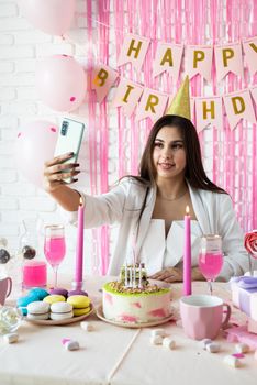 Birthday party. Birthday tables. Attractive woman in white party clothes celebrating birthday taking selfie on mobile