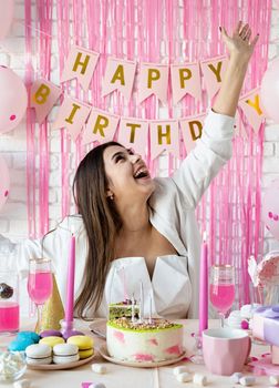Birthday party. Birthday tables. Attractive brunette woman in white party clothes preparing birthday table with cakes, cakepops, macarons and other sweets