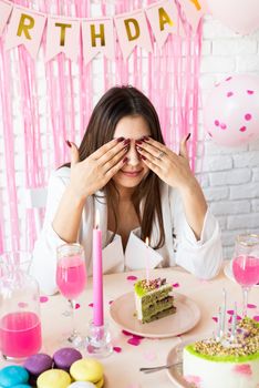 Birthday party. Birthday tables. Attractive brunette woman in white party clothes preparing birthday table with cakes, cakepops, macarons and other sweets, making wish