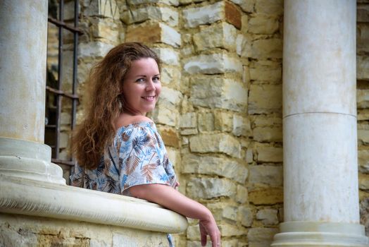 Portrait of young pretty woman on stairs near ancient historical building from stone and seashells.