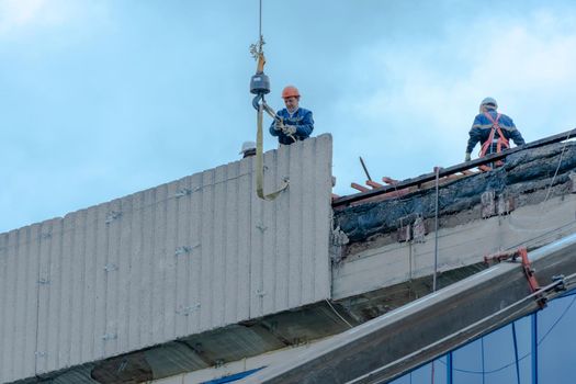 Moscow,Russia,05,10,2021:Restoration,reconstruction and repair of the building.Construction workers in hard hats install concrete slabs on the roof of the structure.Housing Restoration Construction