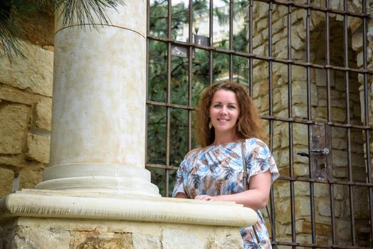 Portrait of young pretty woman on stairs near ancient historical building from stone and seashells.