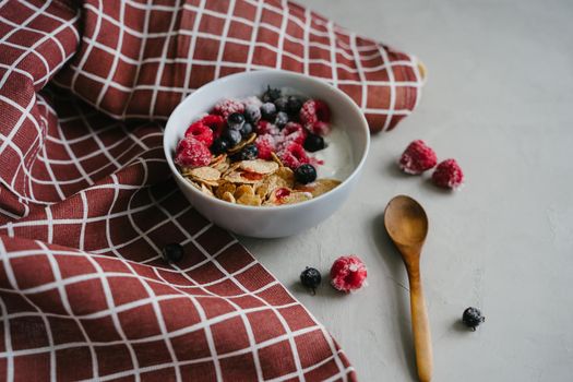 Delicious and healthy breakfast. Natural yogurt, cereals and berries. Hearty breakfast with frozen blackcurrant berries and raspberries. Wooden spoon. Multi-lacquered cereals for breakfast.