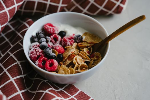 Healthy breakfast with yoghurt, berries and cereals. Wooden spoon. Multi-lacquered cereals for breakfast. Red plaid towel.