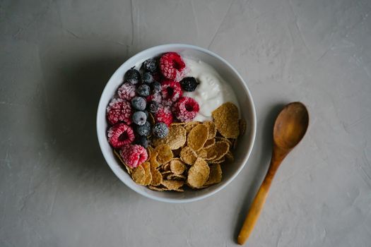 Healthy breakfast with berries, cereals and natural yogurt. Multi-lacquered cereals for breakfast. Berries in ice. Frozen raspberries and black currants. Wooden spoon. Top view.