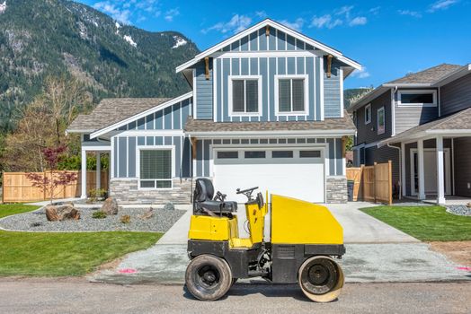Brand new house on the final stage of construction with yellow roller-compactor in front. Family house on snow mountain and blue sky background