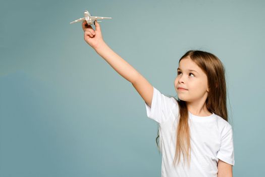Photo of a little happy girl holding a toy airplane. Copy space isolated on blue color background.
