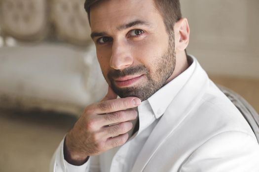 Elegant young handsome man with a beard in a white classic suit.