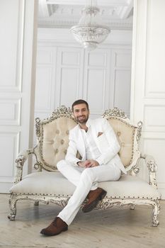 Elegant young handsome man with a beard in a white classic suit.