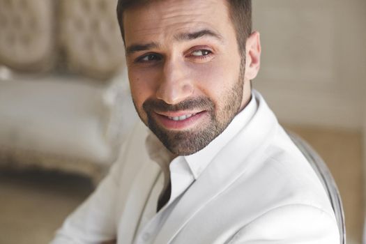 Elegant young handsome man with a beard in a white classic suit.