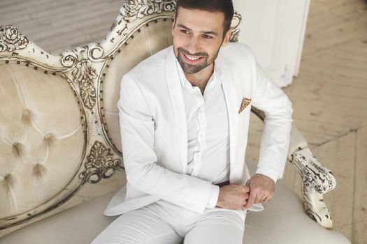 Elegant young handsome man with a beard in a white classic suit.