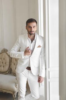 Elegant young handsome man with a beard in a white classic suit.