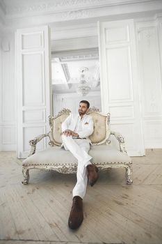 Elegant young handsome man with a beard in a white classic suit.