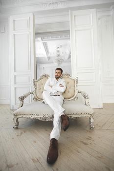 Elegant young handsome man with a beard in a white classic suit.