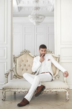 Elegant young handsome man with a beard in a white classic suit.