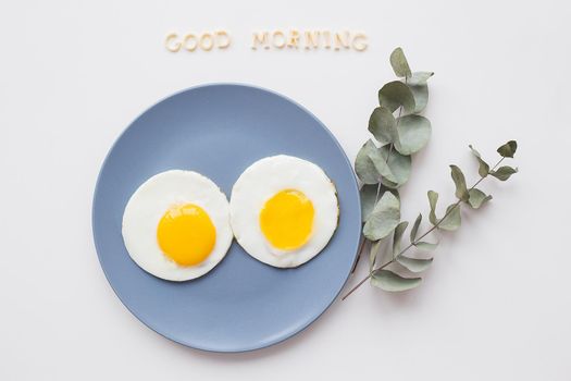 two eggs on a plate with a sprig of eucalyptus, an inscription good morning