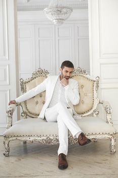 Elegant young handsome man with a beard in a white classic suit.