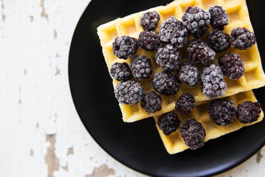 Belgian waffles with blackberries on the old wooden table, close-up.