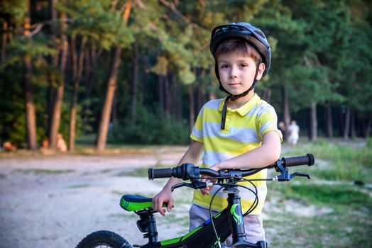 Portrait of happy toddler child boy riding on bike with helmet. He rides from a small hill, through a sandy forest path. Sport concept: kids ride bicycle first bike active toddler kid.