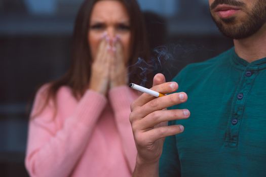 Passive smoking. Man smoking cigarette near woman covering her face from cigarette smoke. High quality photo