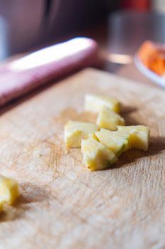 Close-up of pineapple slices scattered above scratched cutting board. Fresh and juicy sliced fruit on wooden surface with blurry background. Healthy meal preparation