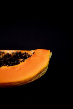 Close-up of half of fresh and tasty papaya laying down on black surface. Juicy sliced fruit with round black seeds above dark background. Healthy food and freshness